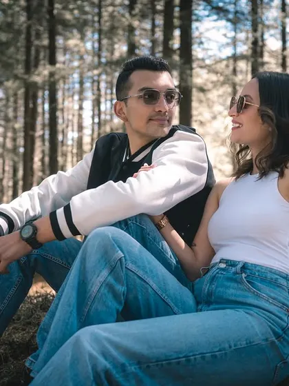A relaxed moment with the couple sitting together on the forest floor, engaged in conversation. This captures the comfortable and casual side of their relationship.