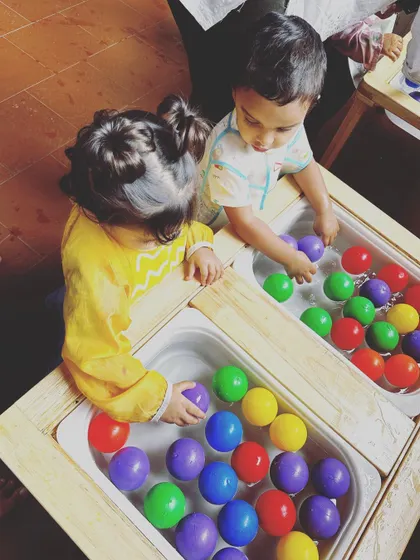 Two toddlers engaged in parallel play at our sensory water stations. They are each exploring the colorful balls in their own bin, learning to share a common space.