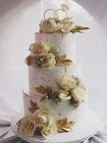 A classic and romantic three-tier wedding cake. I adorned this beauty with cascading off-white roses, baby's breath, and a touch of gold leaf for an elegant and timeless look.
