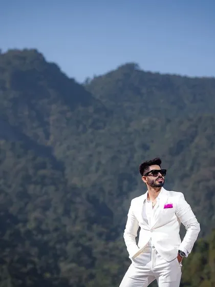 A confident and stylish portrait of the groom against the majestic mountains of Rishikesh. Dressed in a sharp white suit, he exudes modern elegance, showcasing a look that perfectly complements the grand landscape.