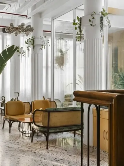 This view showcases the interplay of textures, from the polished terrazzo floor to the fluted white columns and warm wood furniture. Hanging plants and large potted greenery are placed throughout to ensure nature is felt in every corner.