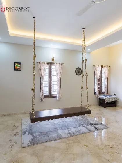 This spacious room features a traditional Indian swing, or 'oonjal', creating a perfect spot for relaxation. The marble flooring and simple false ceiling design add to the room's airy and open feel.