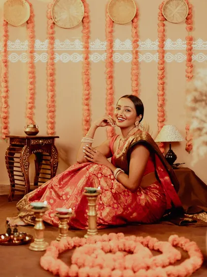 A wide shot that captures the whole festive atmosphere. The model is seated amidst a rangoli of flowers, creating a beautiful, traditional scene.