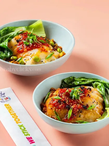 Two bowls of Japanese sticky rice topped with grilled fish and a spicy sauce.