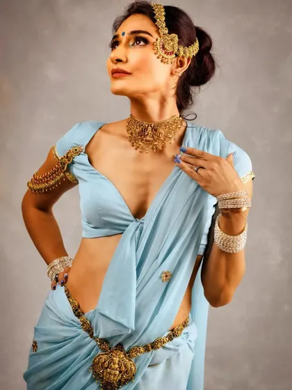 This shot showcases the full look, including the arm cuff and waist belt (oddiyanam). The makeup is designed to complement the entire ensemble without overpowering the magnificent gold jewellery.