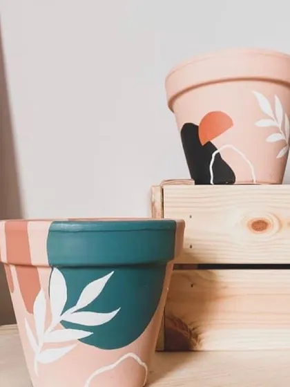 These planters feature abstract botanical designs painted over color-blocked backgrounds. The combination of earthy pinks, deep teals, and leafy whites creates a beautiful statement piece.