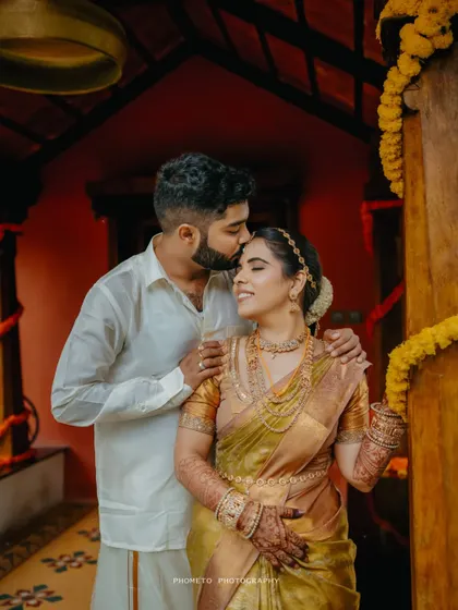 A tender moment as the groom kisses his bride's forehead inside a beautifully decorated traditional home.
