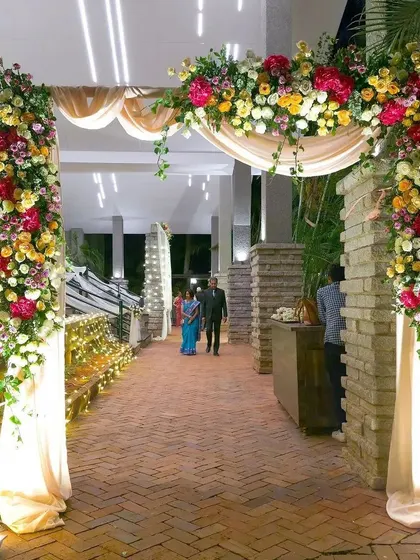 A lush and beautiful floral archway for a wedding entrance. The combination of colorful flowers, green foliage, and soft lighting creates a stunning welcome for your guests.
