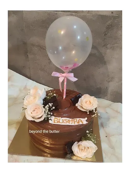 A beautiful chocolate cake decorated with fresh roses and a clear balloon topper for a touch of whimsy.