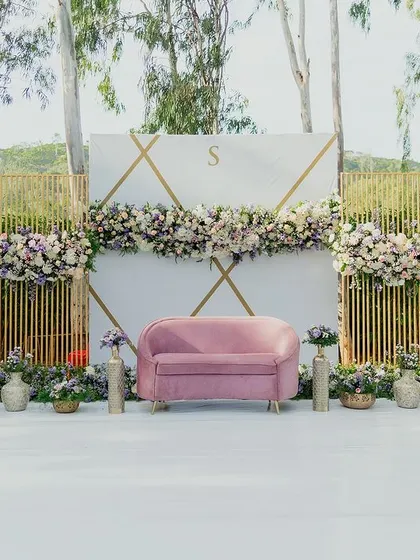 This dreamy, pastel-themed engagement stage was designed to complement the serene beauty of the Chamundi Hills backdrop. The modern, minimalist structure with clean lines, geometric gold accents, and soft floral arrangements in lavender and pink creates a chic and sophisticated atmosphere.