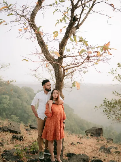 A serene portrait of the couple standing by a tree, with the beautiful landscape stretching out behind them.