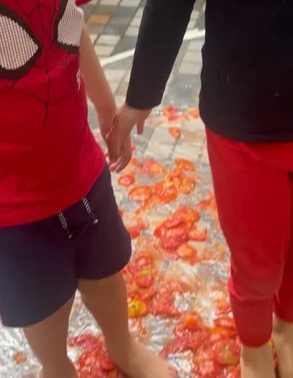 Two children hold hands while squishing tomatoes with their bare feet, a truly memorable sensory experience.