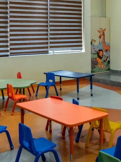 A classroom designed for young learners, featuring brightly colored chairs and tables. The furniture is child-sized and durable, while whimsical animal graphics on the storage cupboards add a playful touch to the room.