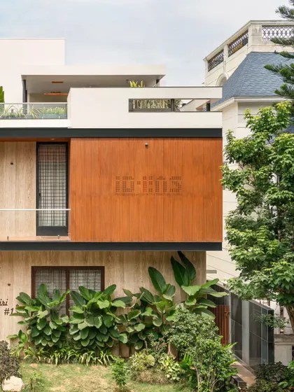 A close-up of the facade, detailing the texture of the wood-finish panels against the smooth white walls and the tropical plants that add a burst of green.