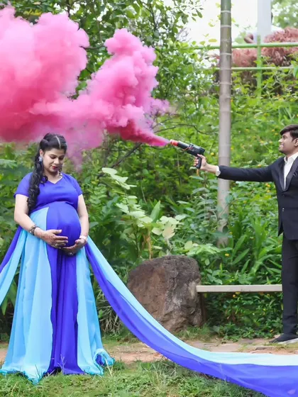 A creative maternity photo using a pink smoke bomb for a dramatic effect. The mother-to-be wears a royal blue and sky blue dual-toned gown with a long trail.