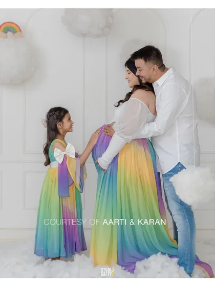 The complete family, including the excited older sister, in matching rainbow-themed outfits. It's a heartwarming portrait of a family growing with love.