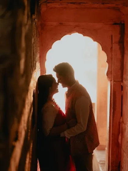 A silhouette of a couple sharing an intimate moment within a stone archway in Jaisalmer. The warm, glowing light creates a romantic and mysterious atmosphere, perfect for a heritage pre-wedding shoot.