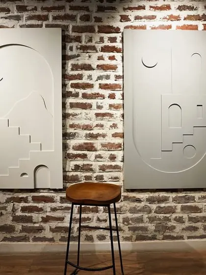 The 'Ashta Prahar' wall murals displayed against a rustic brick wall. The contrast highlights the clean, modern lines of the sculpted panels.