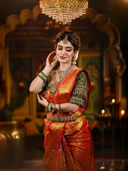 A regal and traditional bridal look featuring a rich red and green Kanjivaram saree. The makeup is defined by warm, shimmery eyes and a deep red lip, perfectly accessorized with temple jewelry.