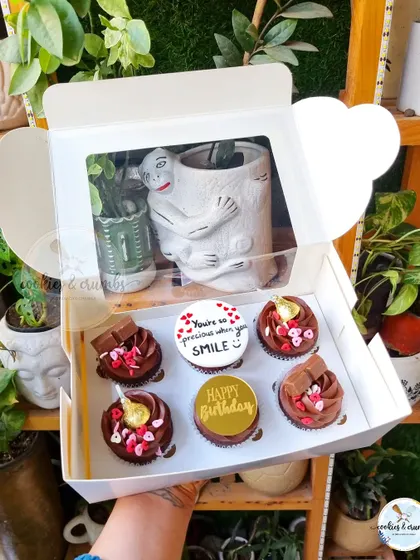 A box of custom chocolate cupcakes. This set includes a personalized message, a birthday wish, and decorations like mini chocolate bars and gold leaf.