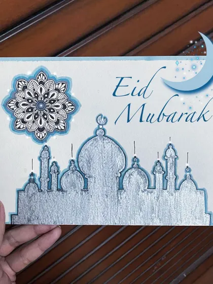 An Eid Mubarak greeting card I designed, featuring a silver silhouette of a mosque and a detailed blue and black mandala. The silver paint gives the piece a festive, metallic shine.