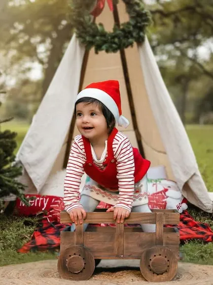 A very merry Christmas shoot. This little one is full of holiday cheer in her Santa hat, enjoying a festive outdoor setup with a teepee and presents.
