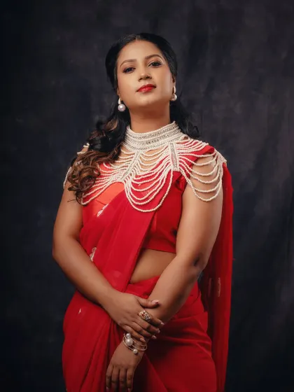 A powerful and elegant portrait in a red saree. The addition of a pearl shoulder piece adds a unique, high-fashion element to the traditional attire.