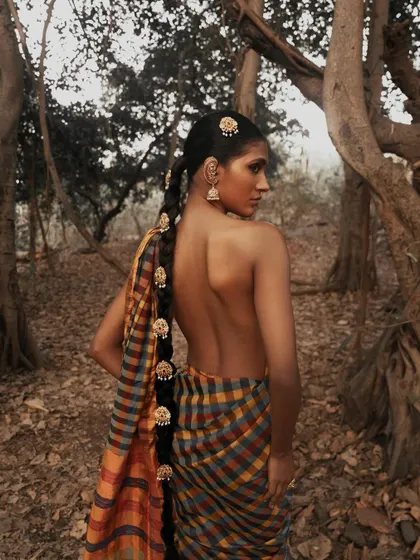 A beautiful three-quarter back view, showcasing the intricate braid and the elegant drape of the saree in a natural, serene environment.