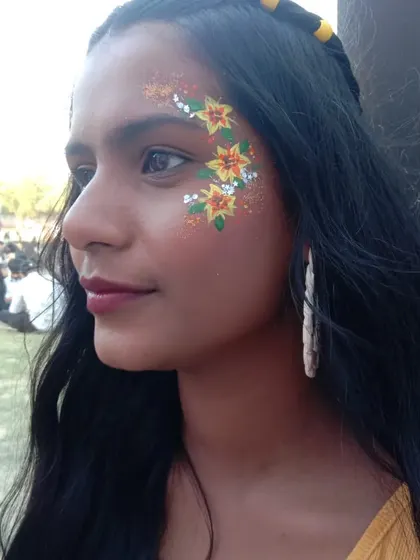 Bright and sunny yellow lily flowers painted along the cheekbone, accented with orange and white details and a dusting of gold glitter.
