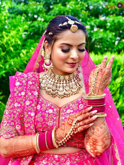 A beautiful outdoor bridal portrait. The bride, dressed in a vibrant pink lehenga, shows off her intricate mehndi with a playful gesture.