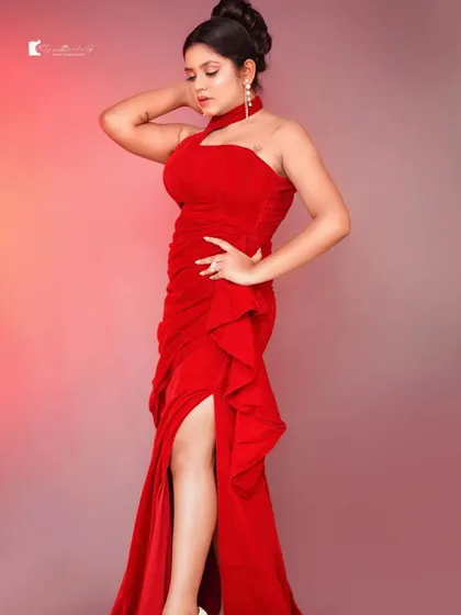 A model showcasing the elegant silhouette of the red halter-neck gown. The ruching on the side and the ruffled slit add texture and drama.