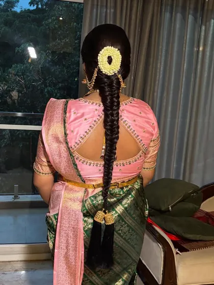 A neat, traditional braid with a jasmine gajra and decorative tassels, perfectly complementing the client's pink and green silk saree.