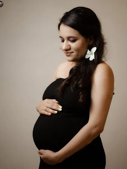 A simple and elegant solo portrait. The mother-to-be is looking down at her bump, creating a tender and personal moment, enhanced by the clean, neutral background.