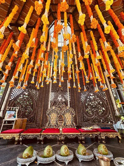 A traditional Muhurtham stage with a ceiling of hanging marigold garlands and ornate carved wooden screens, perfect for a heritage-themed wedding.