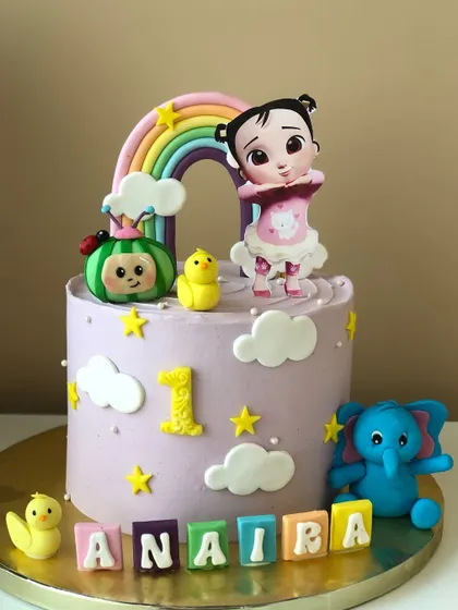 A sweet Cocomelon cake for a first birthday, featuring a pastel rainbow and characters from the show.