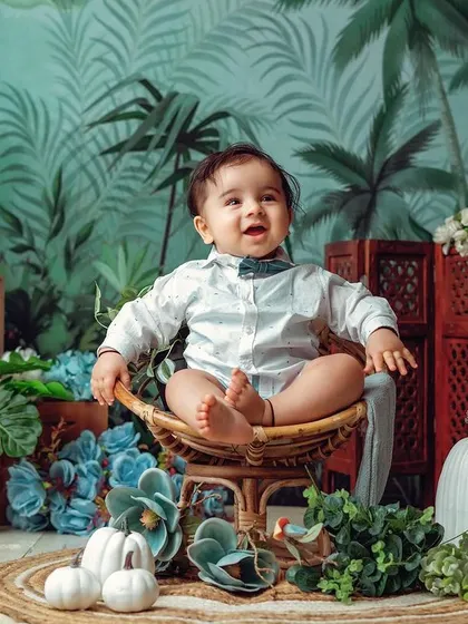 This little pumpkin is sitting like a pro. The tropical leaf background and wicker chair create a stylish and modern sitter portrait.