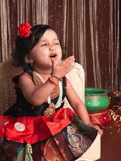 A thoughtful moment from our little Krishna-themed shoot. The details, from the red flower in her hair to the decorated pots, make this festive setup so special.
