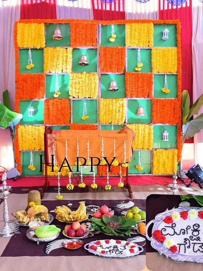 This photo shows a complete setup for an Annaprasanna (first rice-eating ceremony) with a colorful marigold backdrop and the traditional arrangement of food and offerings in the foreground.