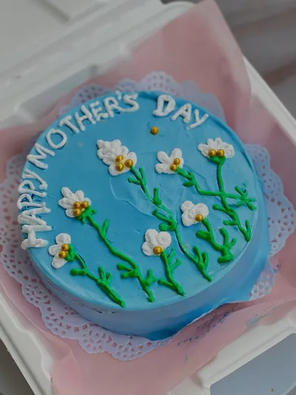This beautiful blue bento cake features hand-piped floral designs. It's a small but heartfelt way to say 'Happy Mother's Day' with a delicious, personal-sized cake.