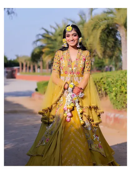 A full-length shot of the bride in her stunning yellow Haldi lehenga. The outdoor setting with palm trees adds a destination wedding feel to this vibrant pre-wedding ritual.