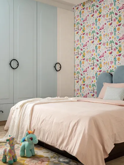 A different view of the kid's room, showing the custom-designed pale blue wardrobe with classic circular handles. The design seamlessly integrates storage with the playful flamingo wallpaper and soft-hued bedding.