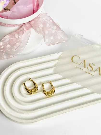 A pair of textured gold hoop earrings styled on a modern tray. The simple composition and bright lighting make the product details pop.
