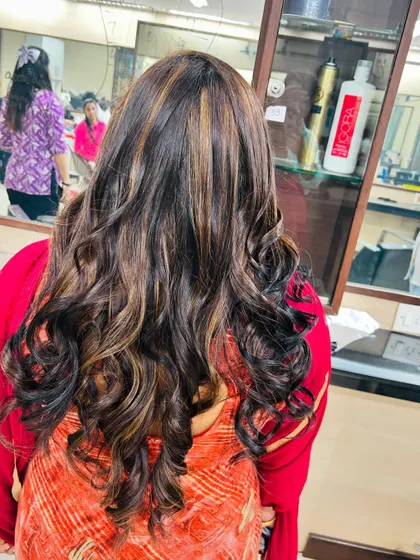A beautiful example of a global hair color combined with subtle blonde highlights. This look, finished with soft curls, demonstrates a classic and highly sought-after salon service.