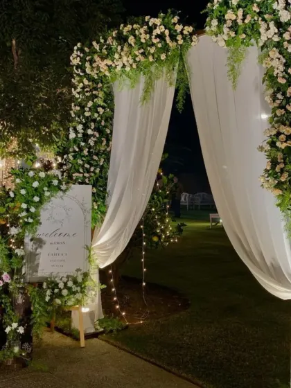 An enchanting nighttime entrance with a floral arch, sheer white drapes, and a beautifully lit welcome sign.