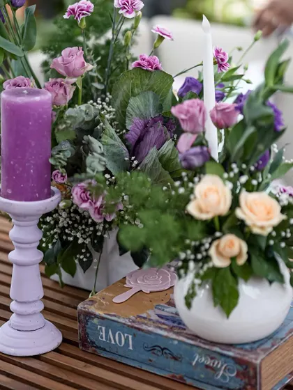 A close-up of a table centerpiece from the 'Victorian Bageecha' mehendi, featuring a purple candle and a mix of pastel flowers.