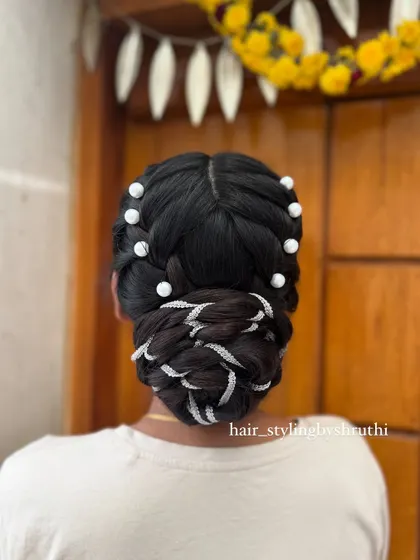 A braided bun hairstyle where the braids are interwoven with a silver ribbon and accented with large pearls. This updo combines traditional braiding with modern accessories for a unique look.