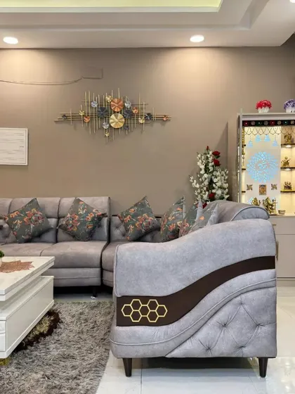 A comfortable living room setup with a grey sectional sofa, floral cushions, and a small pooja unit, demonstrating our ability to blend everyday comfort with spiritual elements.