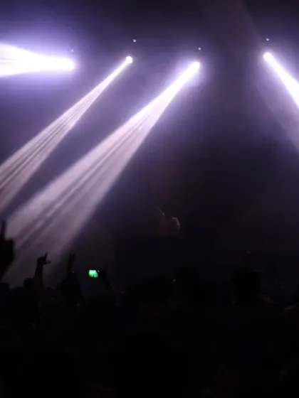 A dramatic, low-light shot of the crowd with spotlights focused on the stage, creating a classic concert feel.