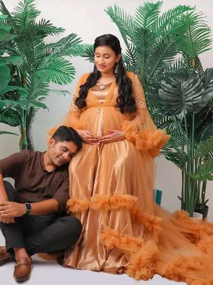 A tender moment between a couple in our studio. The father-to-be rests his head on the baby bump, surrounded by lush greenery props and the mother's stunning golden gown.