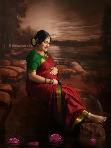 A serene portrait set against a painted backdrop of a river scene, with the mother-to-be looking down at her bump with love.